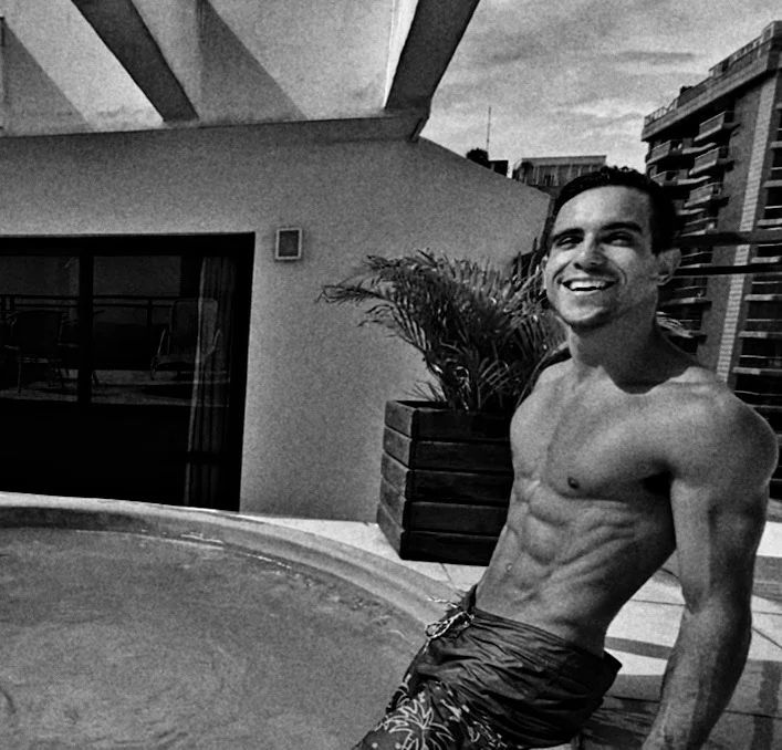 Black and white photo of Raphael smiling by a rooftop pool