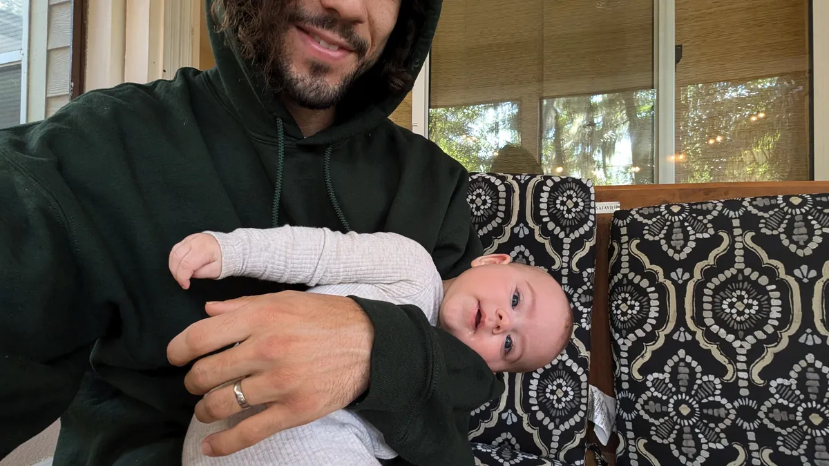 Raphael in a green hoodie holding his baby daughter