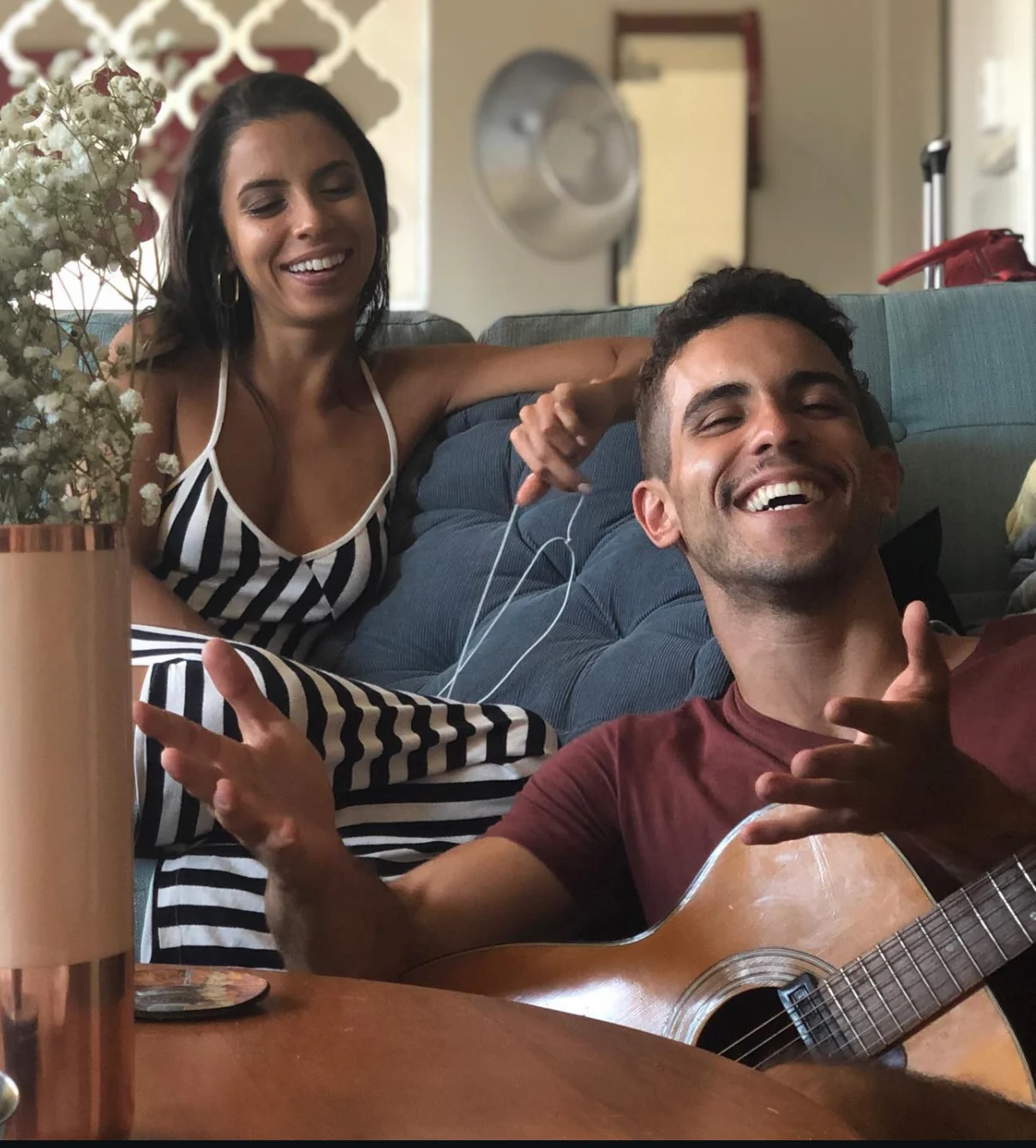 Raphael laughing while playing an acoustic guitar on a couch