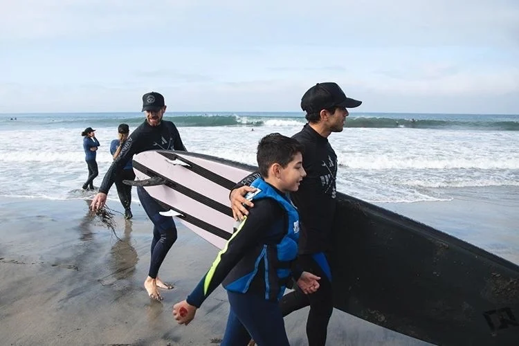 Surf instructor walking a young surfer along the beach carrying boards