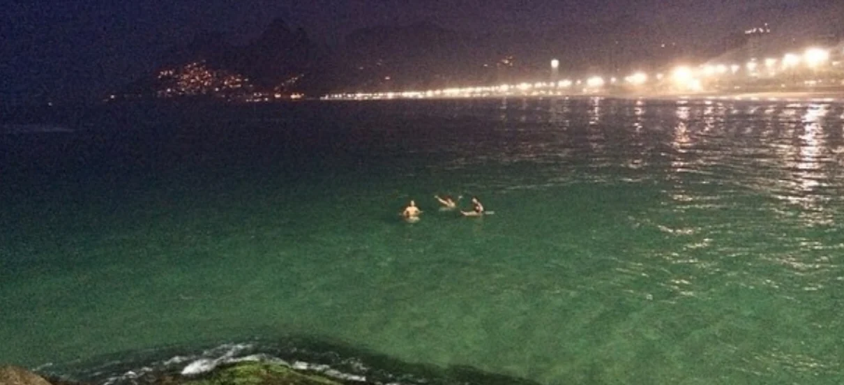 Swimmers in the night sea with city lights along the coast