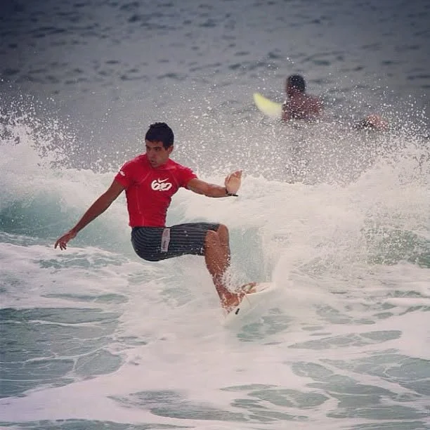 Raphael surfing a wave in a red rash guard