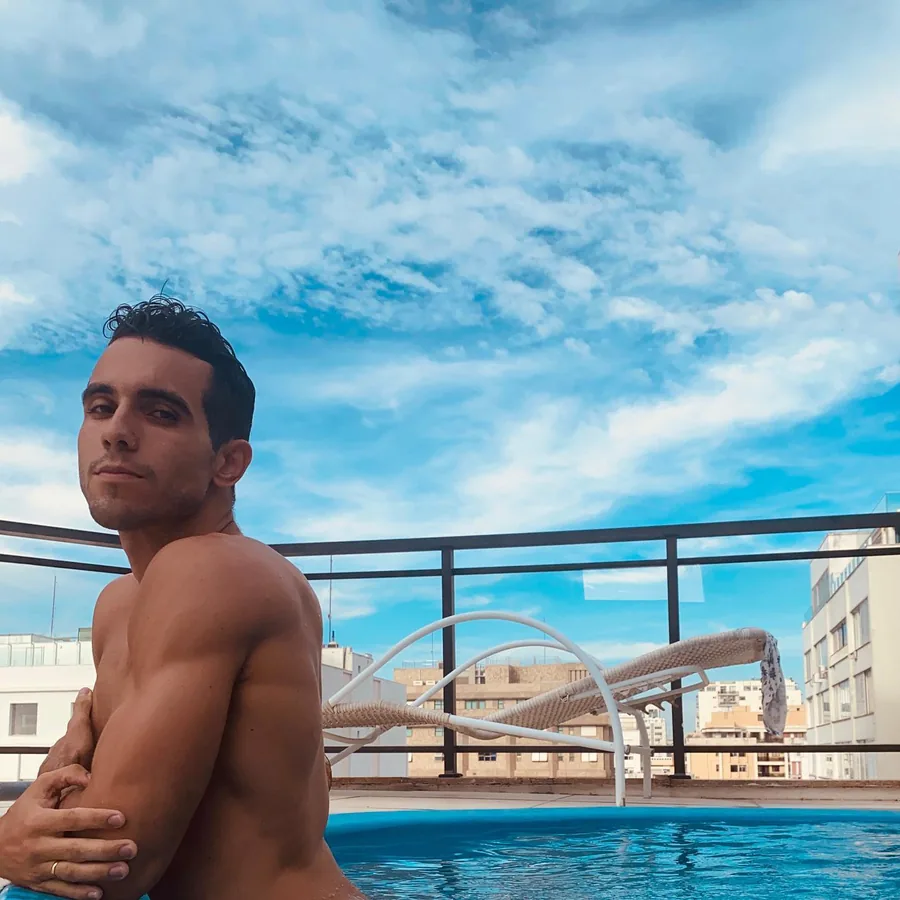 Raphael shirtless at the pool under a blue sky