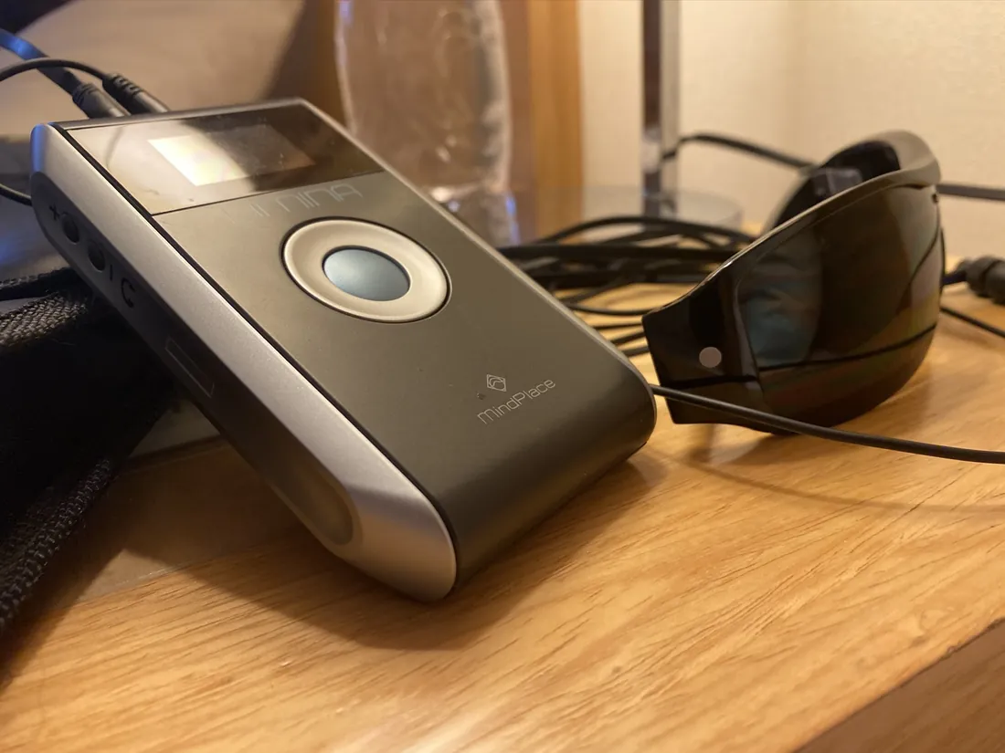 A light and sound relaxation device with eye goggles resting on a wooden nightstand