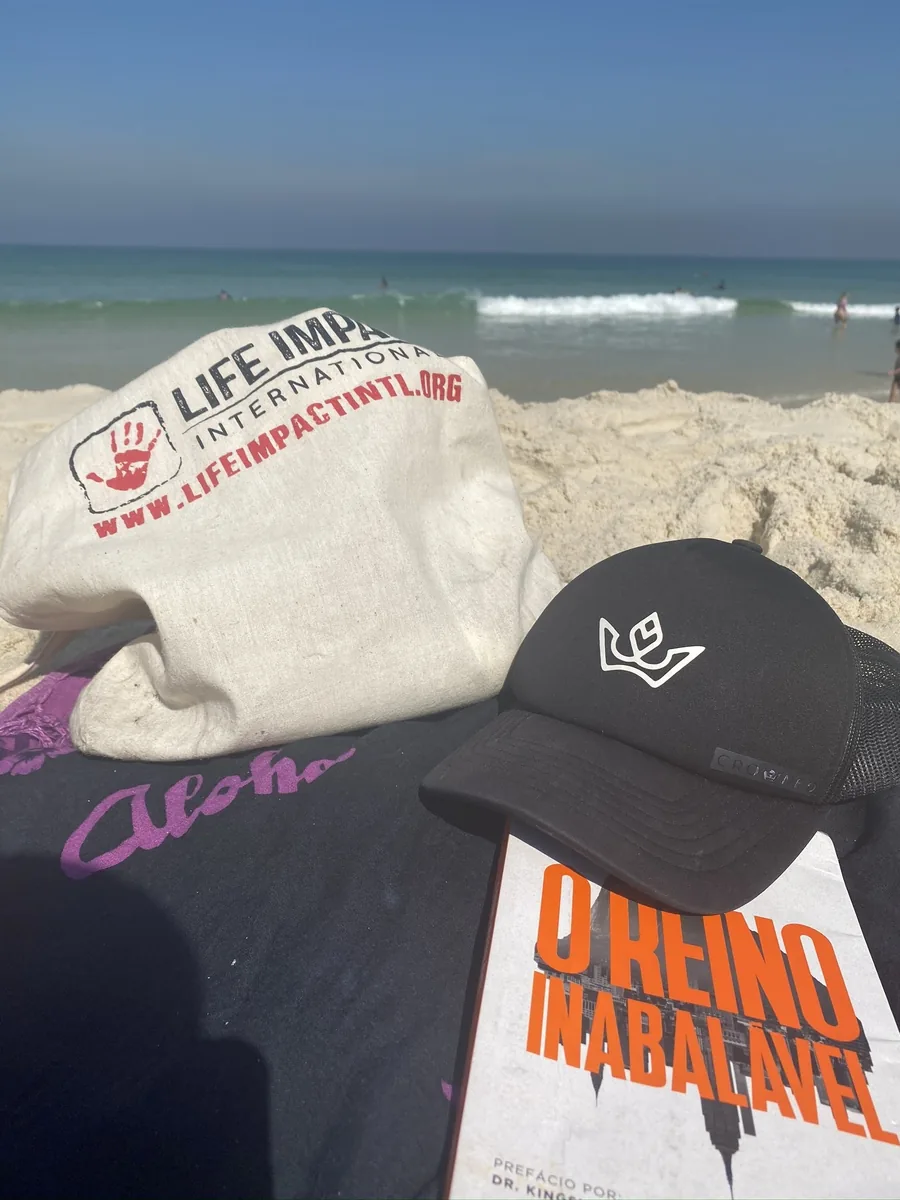 A beach scene with a canvas tote bag, a black cap and a book resting on the sand
