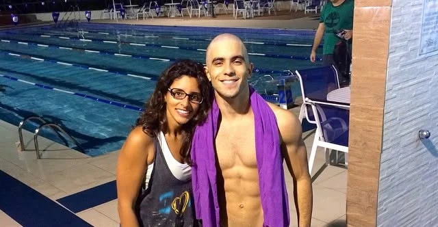 Raphael at the pool in swim trunks with a purple towel, next to a client