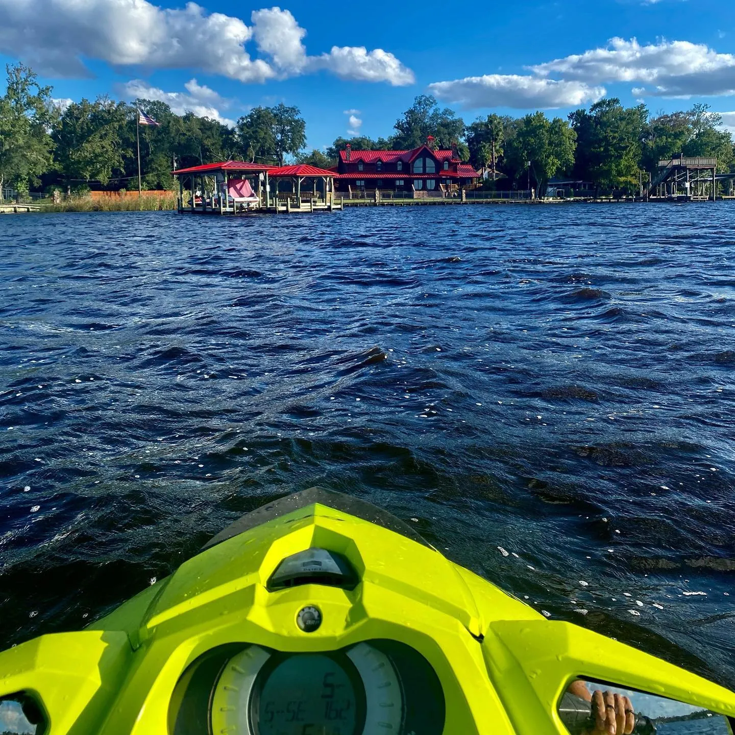 View from a yellow jet ski across a choppy lake toward a red-roofed boathouse